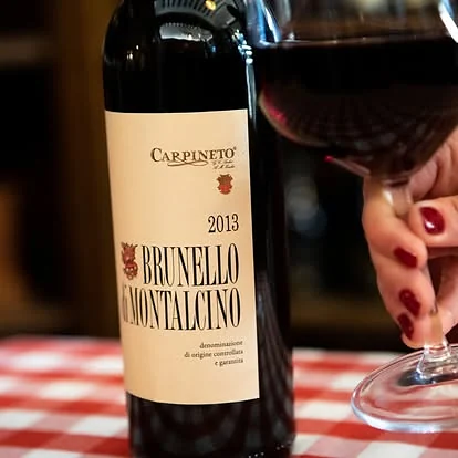 Bottiglia di Brunello di Montalcino e calice di vino rosso sulla tovaglia a quadretti